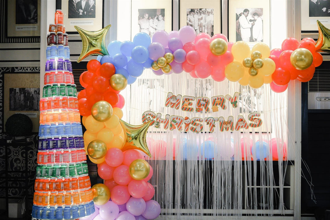 Christmas tree built from Goli gummy jars beside a pastel balloon arch and Merry Christmas backdrop
